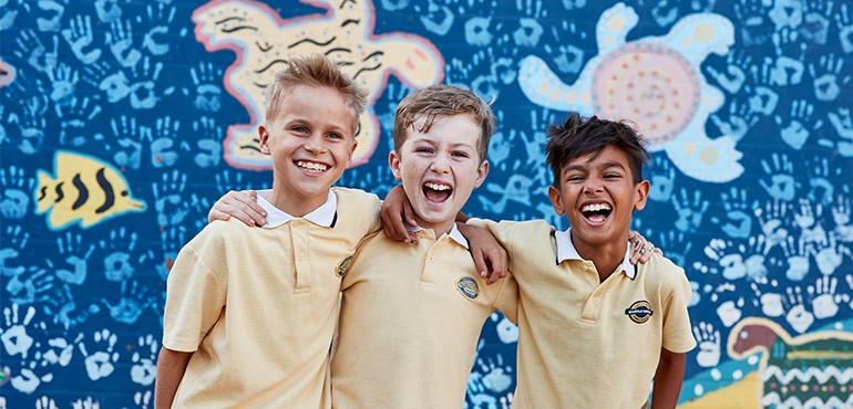 Three boys smile with their arms around each other.